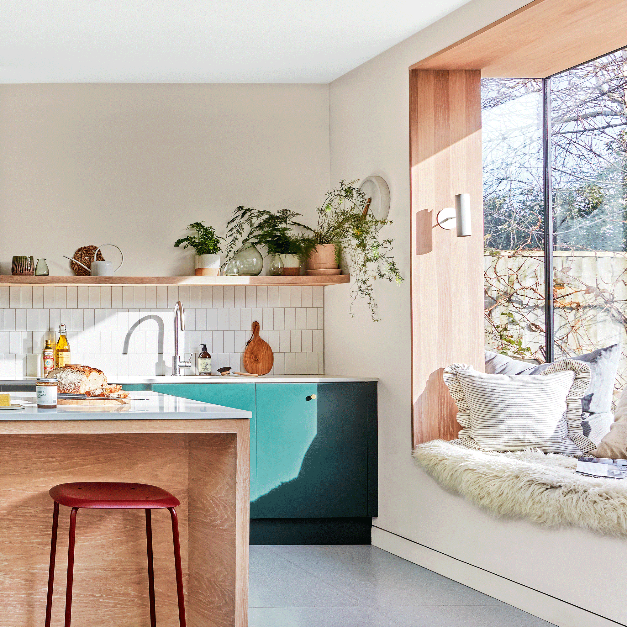 a neutral kitchen with green cabinets and a large picture window with window seat covered in comfy cushions