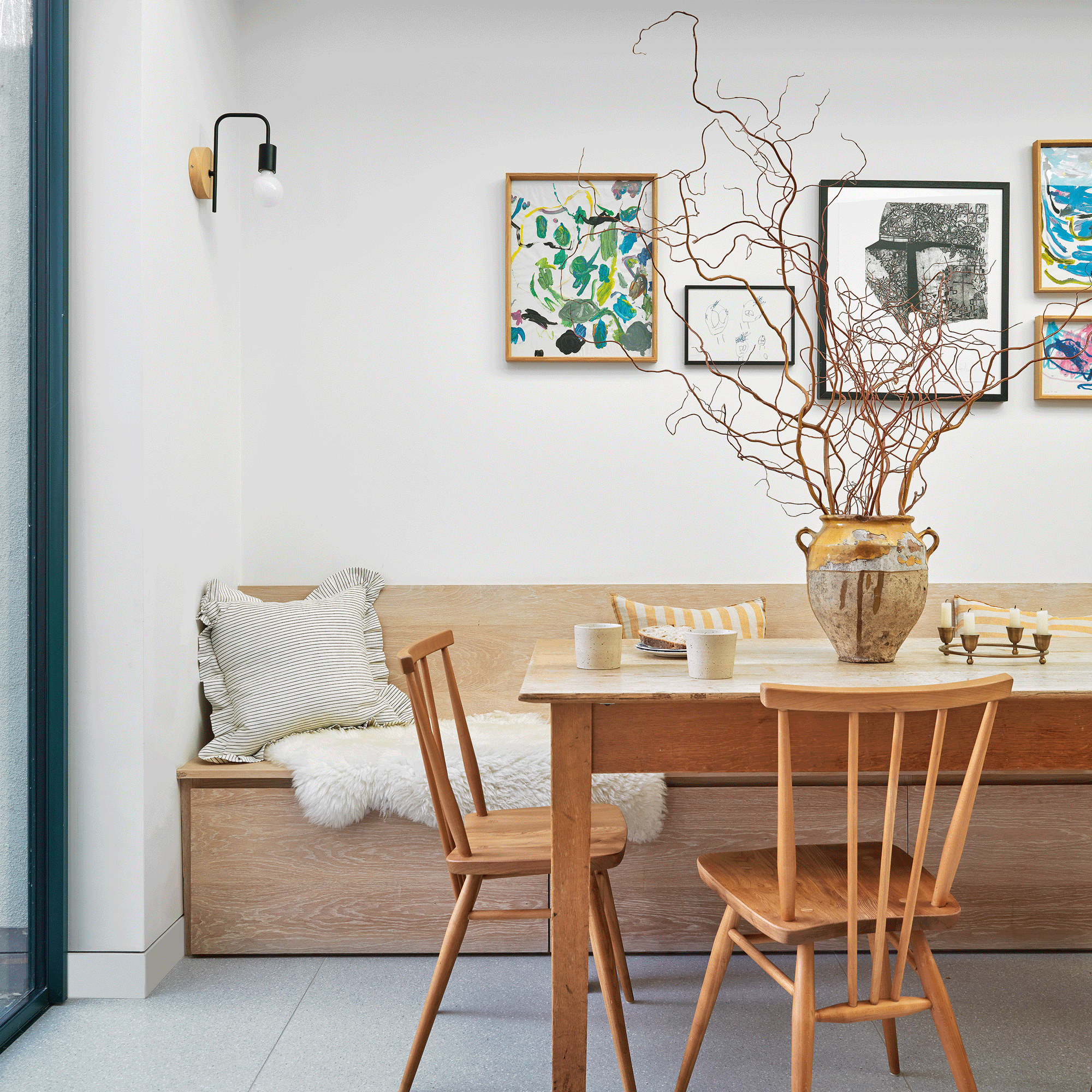 a dining area with built-in banquette seating bench a wooden dining set and a white wall with a selection of framed prints