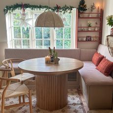 Striped kitchen banquette seating around round wooden table with Christmas decor on the walls