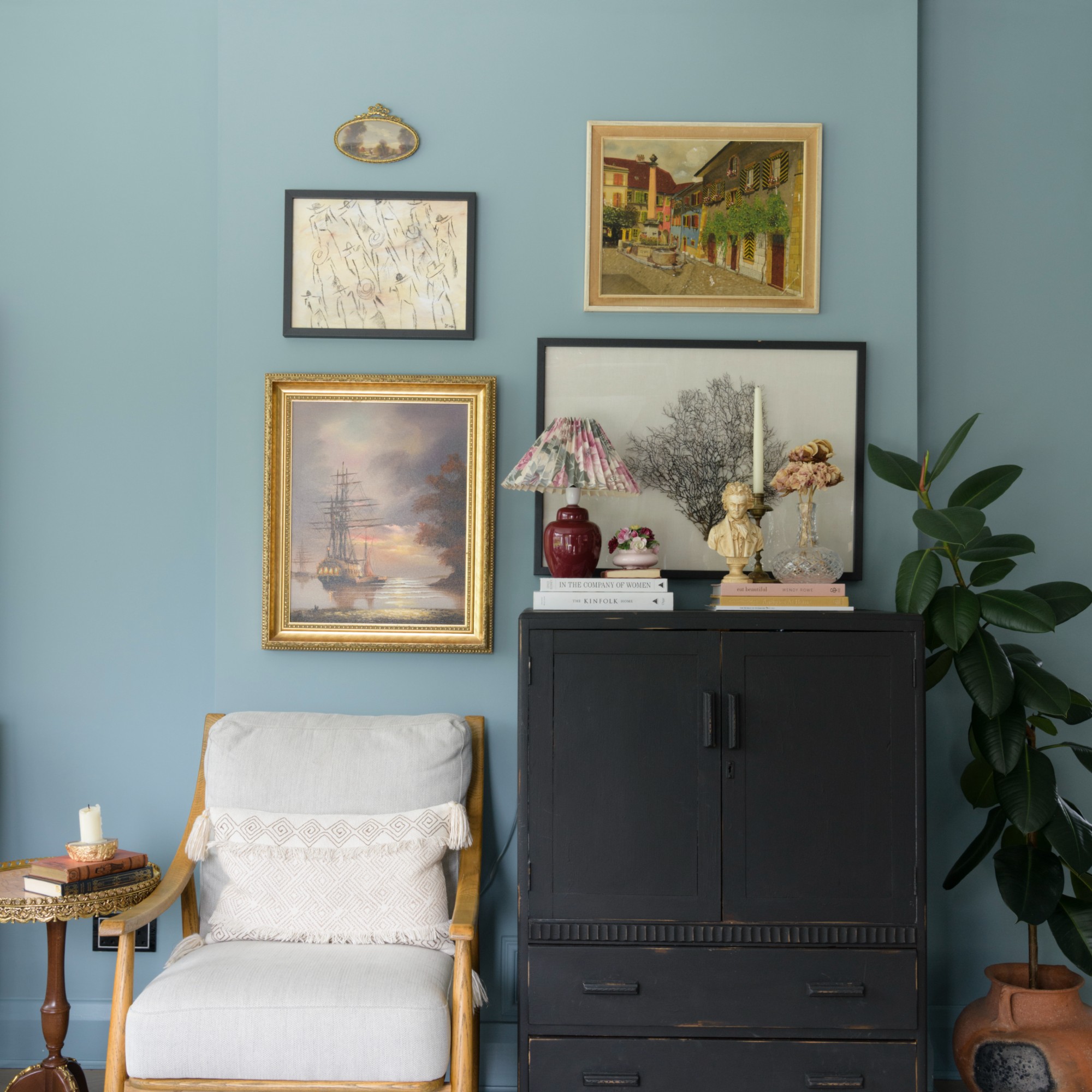 A blue-painted living room with a small gallery wall and an antique black cabinet