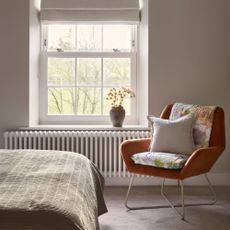 Bedroom with an orange accent chair sitting by the window, with a white radiator underneath it