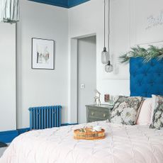 White bedroom with a blue radiator, blue skirting board and blue headboard.