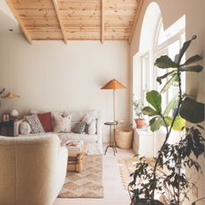 A while living room with high ceilings and a cream linen sofa, jute rug and a teddy-finish armchair in cream