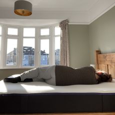 A woman lying on her side on the Nectar Premier Hybrid Mattress in front of a bay window in a bedroom