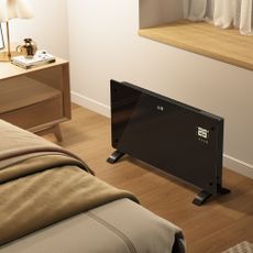 2000W smart panel electric heater from Vonhaus on the floor next to a bedside table in a bedroom