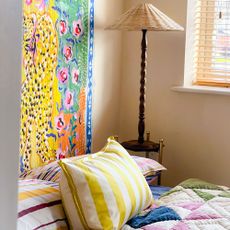 Bedroom corner with tall wooden table lamp and colourful print behind bed