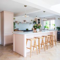 pink kitchen with a large kitchen island, three ceramic pendants overhead and a breakfast bar with four stools
