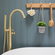 Close up of a gold bath tap in front of a dark blue panelled wall.